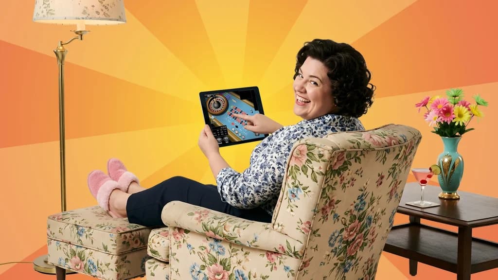 Wearing fuzzy pink slippers and leaning back in her flowery chair, a lady enjoys a game of online roulette in her home. 