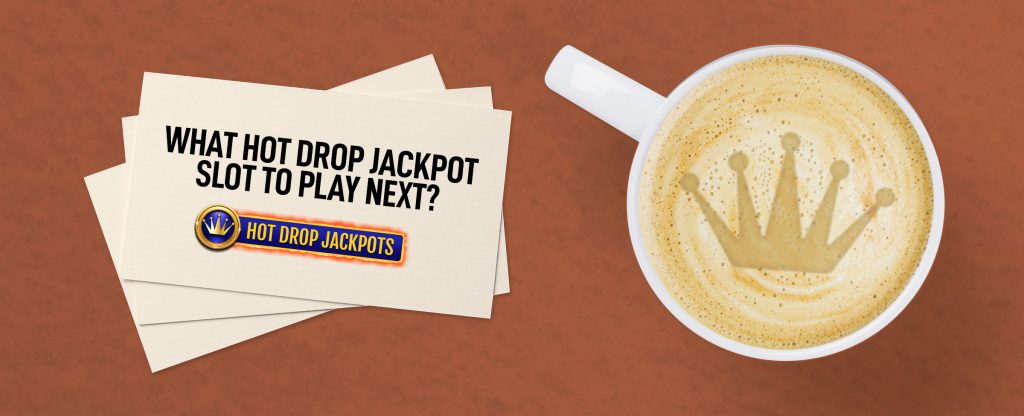 A coffee mug filled with a latte and an emblem of a crown sits on a brown table, next to three cards, the top one reading “What hot drop jackpot slot to play next?”, featuring the Cafe Casino Hot Drop Jackpots logo beneath it.