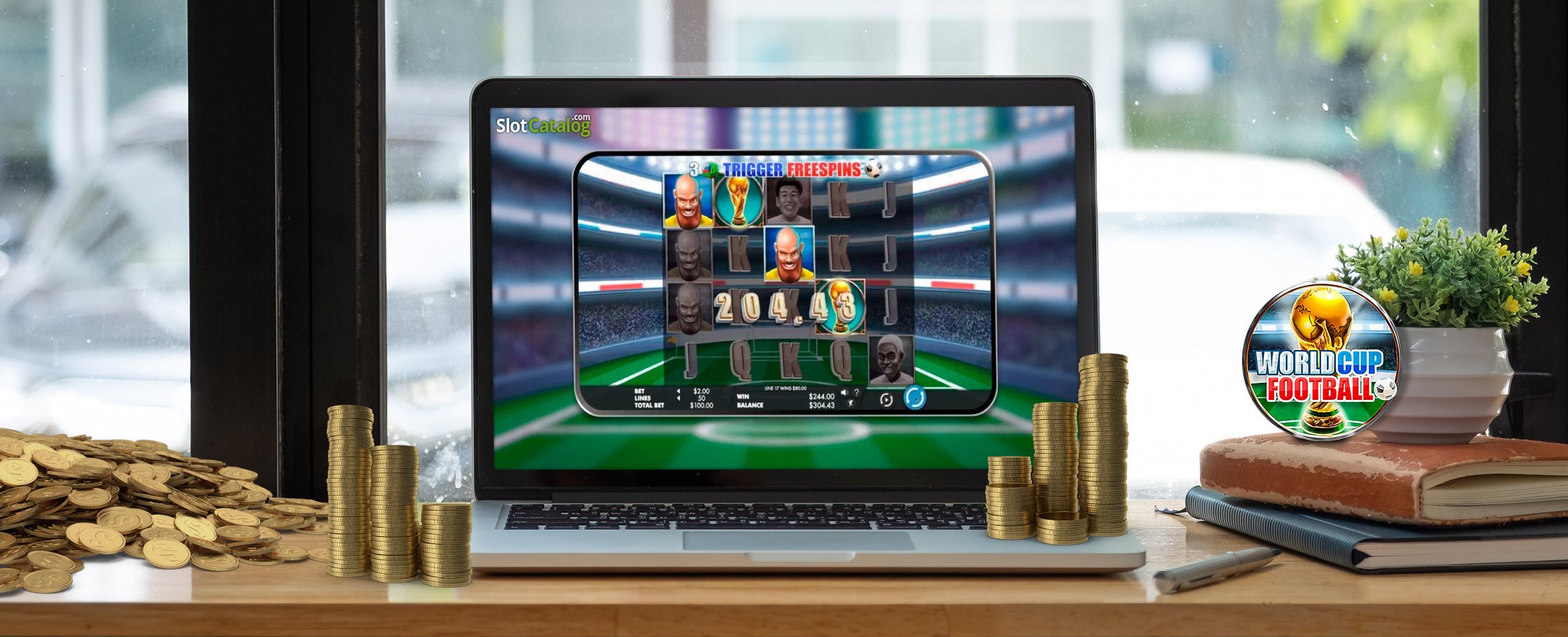 A wooden counter bench is pictured with a MacBook sitting on top, open, previewing the Cafe Casino slot game “World Cup Football”. Sitting on top of the laptop’s keypad is a stack of coins, sitting next to two books propping up a small plant. Over on the left is a pile of gold coins.