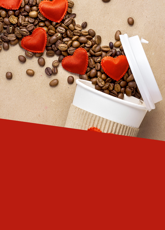 A white reusable coffee cup, partially obscured by a red overlay, is seen placed on its side on top of a beige benchtop, with coffee beans spilling out, accompanied by red-covered heart-shaped chocolates.