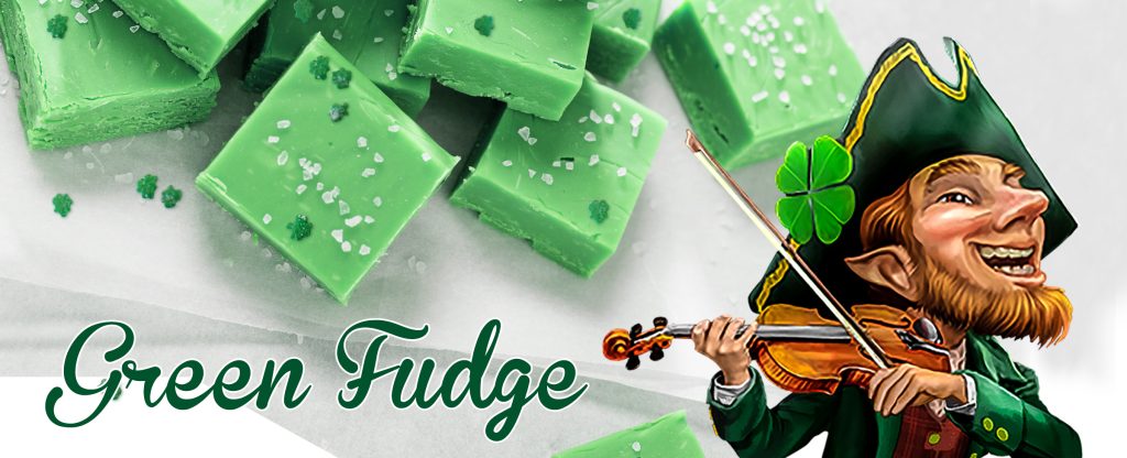 Squares of green-colored fudge sit on a white plate, sprinkled with sugar and coloring. To the right, the main illustrated leprechaun character from the Cafe Casino slot game, Leprechaun Legends, is wearing a green suit, bushy beard, a hat with a four-leaf clover, and holding a fiddle. To his left are the words, Green Fudge.