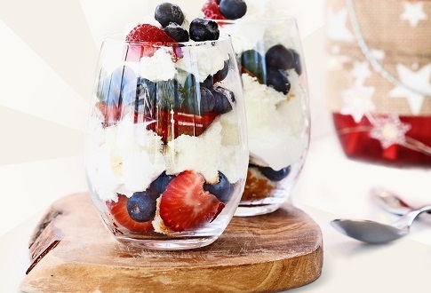 Two glasses on top of a wooden platter filled with trifles, in the fourth of July colors, featuring strawberries and blueberries surrounded by freshly whipped cream.
