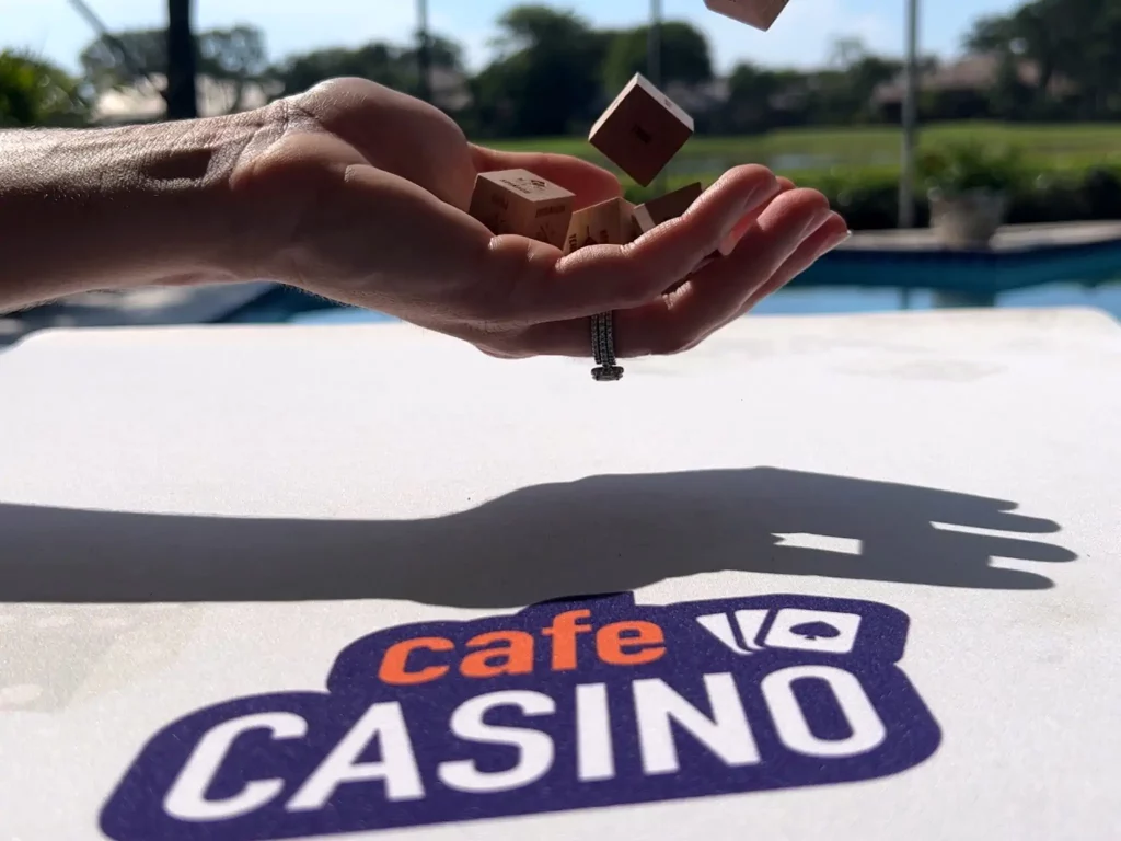 The bottom side of the image features the logo for the online casino, Cafe Casino, and a hand rolling dice with food groups on it.