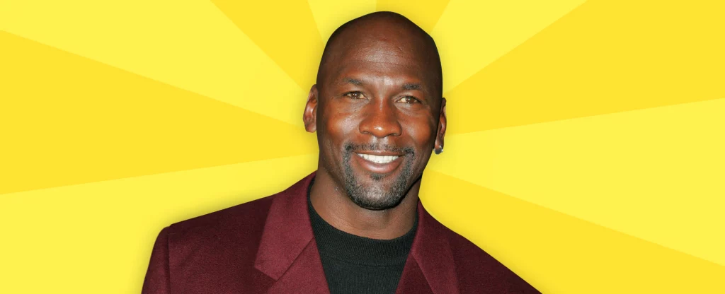 Michael Jordan from the waist up in a maroon coat and a black t-shirt, smiling, set against a yellow striped background.