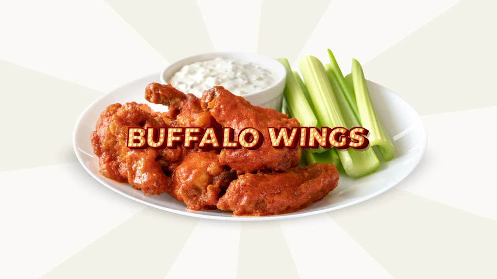 A plate of buffalo wings with a small white dish of sauce and celery sticks sits underneath the words ‘Buffalo Wings’, set against a cream color background.