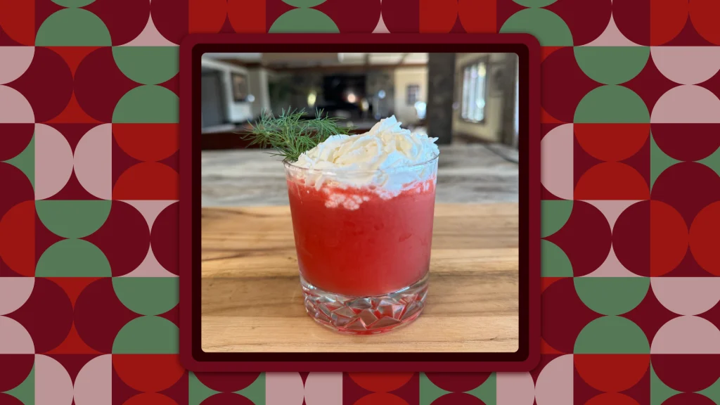 Johnny Drinks’ recipe for the Senor Santa Cocktail is in a glass tumbler, featuring pink color liquid with white whipped cream on top and a garnish of green rosemary.