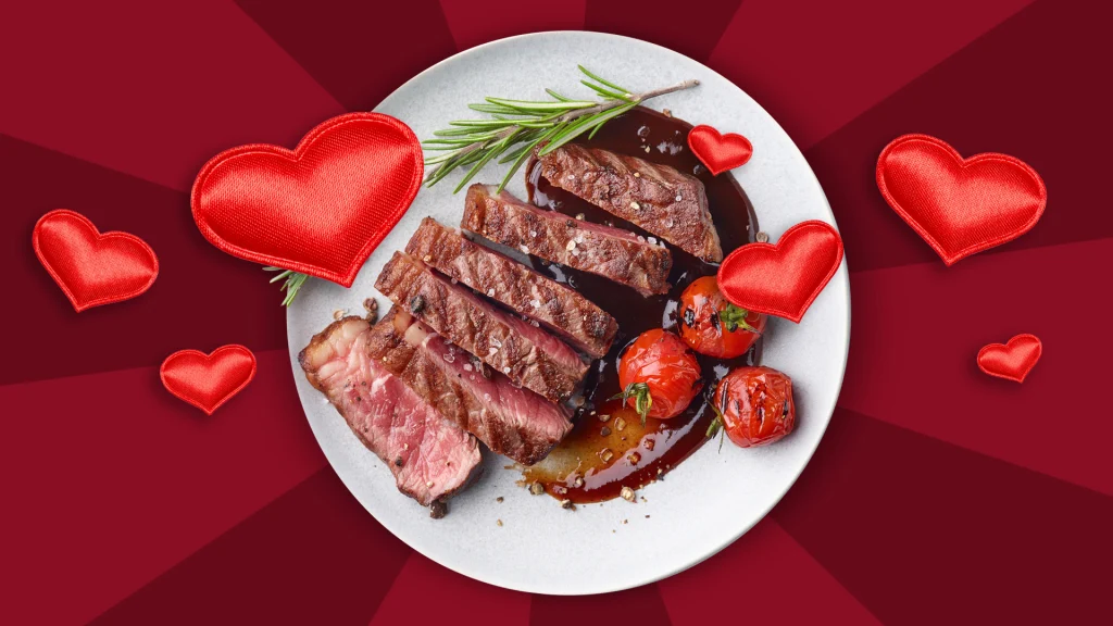 A dish served with a steak sliced up, tomatoes and sauce surrounded by love hearts, on a red background.