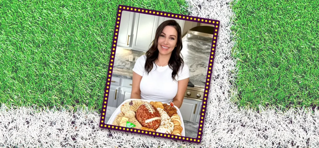 Chef Genevieve stands in a white t-shirt, holding a platter featuring a football shaped cheese ball in the middle, surrounded by crackers.