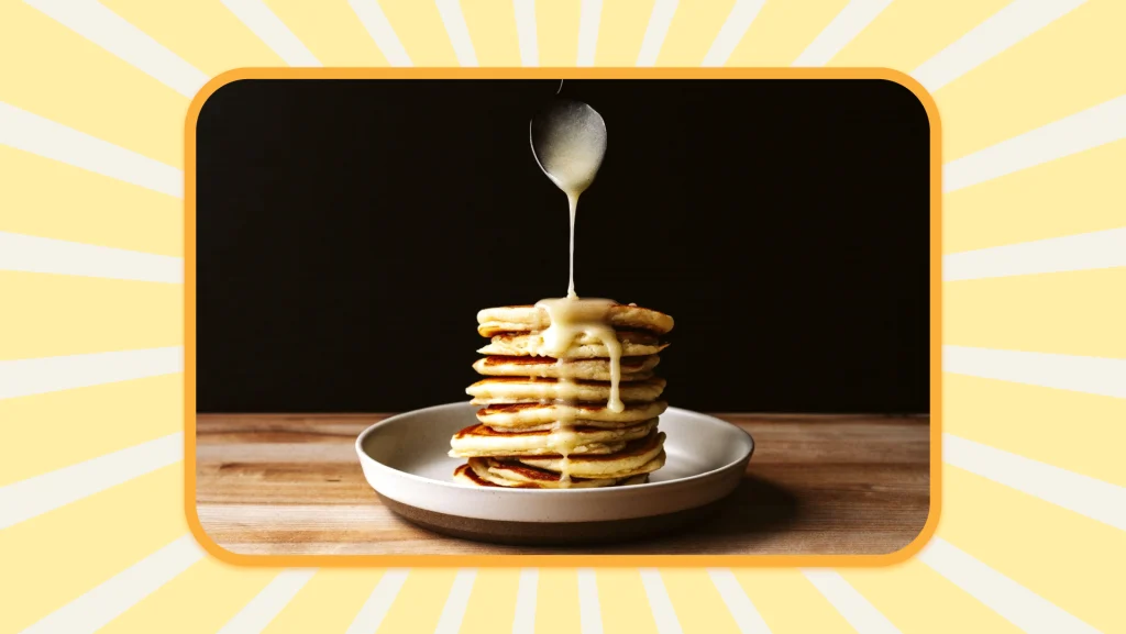 A spoon drizzling lemon curd sauce from above a tall stack of lemon ricotta pancakes.