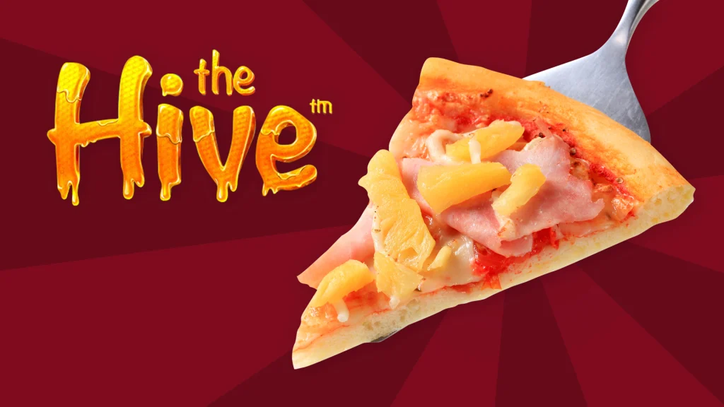 Words read ‘The Hive’ – a Cafe Casino online slot – next to a slice of Hawaiian pizza and both are on a dark red background. 