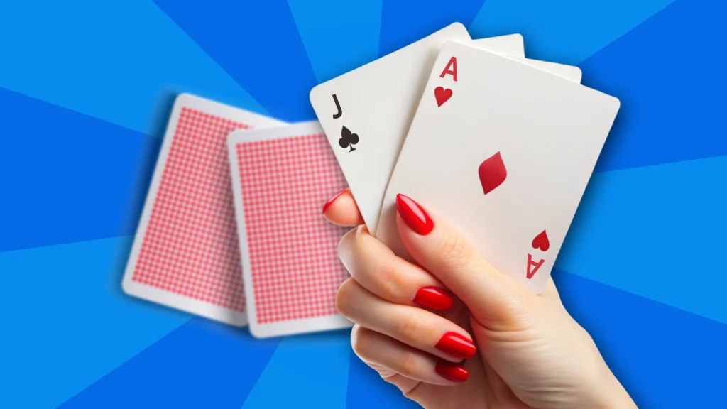 A hand with red nails is holding up two cards - a J and an A. Behind that hand are two more red cards face down, and it’s all on a blue image.