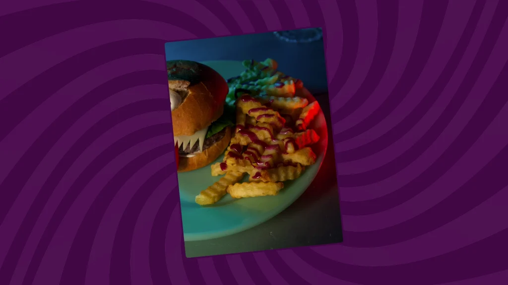 crinkle cut fries sit next to a burger with blueberry ketchup poured over