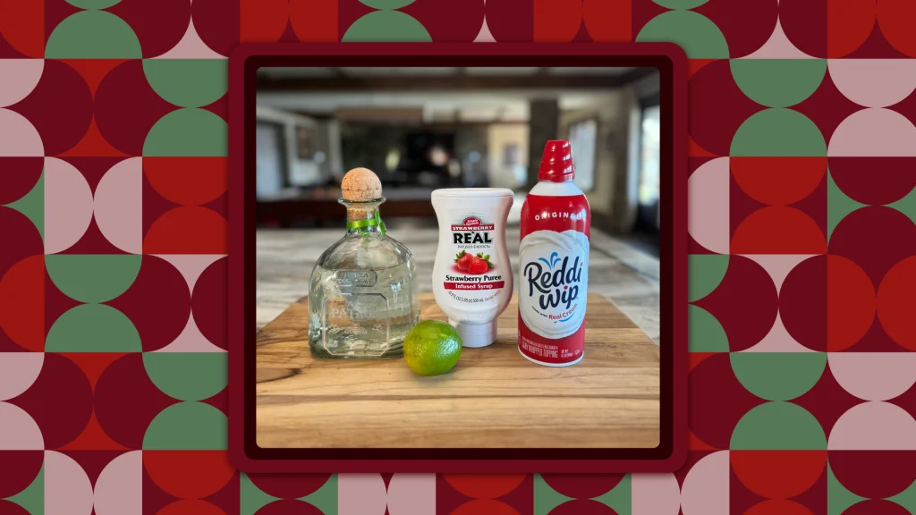 The ingredients for the Senor Santa Cocktail Recipe by Johnny Drinks including a decanter of Blanco Tequila, strawberry pureé in a white bottle, whipped cream in a red canister, and a lime; all positioned on a cutting board.